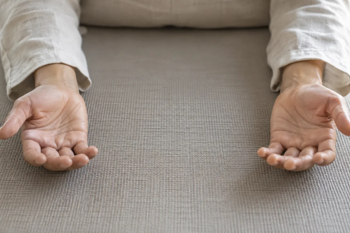 Mains détendues, paumes tournées vers le ciel, posées de chaque côté du corps sur un tapis