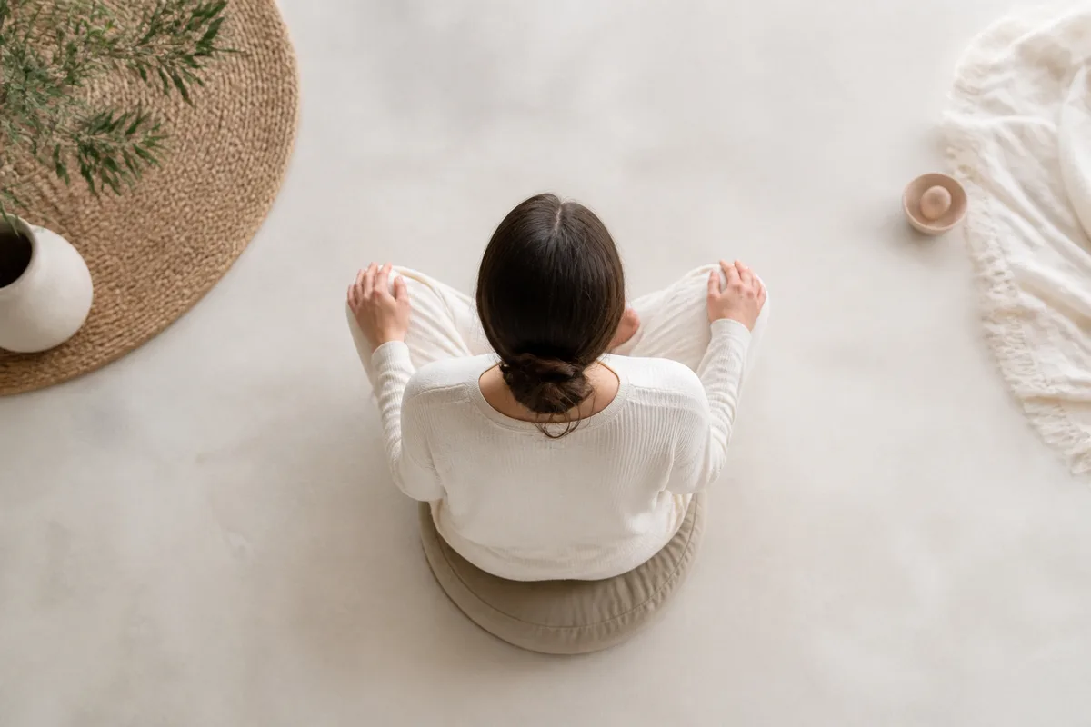 Personne assise en tailleur sur un coussin de méditation, dos droit, mains posées sur les cuisses